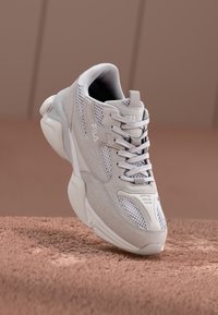 Light gray athletic sneaker featuring mesh panels, textured suede, and a cushioned sole. Laces are prominent, with a small logo detail.