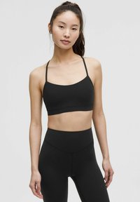 Schwarzer Sport-BH mit dünnen Trägern, nahtlosem Design und weicher Textur. Kombiniert mit hochgeschnittenen schwarzen Leggings. Schlichte, figurbetonte Silhouette.