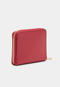 Billetera cuadrada de cuero rojo con un zipper dorado en el borde, mostrada sobre un fondo blanco liso.