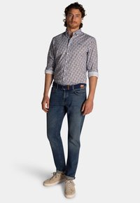 Herenoverhemd met een bloemenpatroon in tinten blauw en bruin, gecombineerd met donkerblauwe denim jeans en lichtgekleurde sneakers.