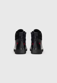 Le sneaker alte nere presentano una costruzione in pelle e camoscio con ricamo a forma di cuore rosso sul tallone e una suola in gomma testurizzata.