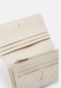 Billetera beige de cuero sintético con un patrón acolchado, que cuenta con múltiples ranuras para tarjetas, un compartimento con cremallera y herrajes en tono dorado.
