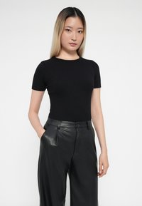 Zwart geribbeld shirt met korte mouwen, gecombineerd met hoge zwarte leren broek. Glad materiaal; getailleerde pasvorm; klassieke ronde halslijn.