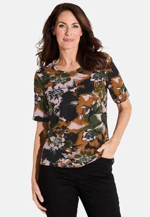 Haut à manches courtes avec des motifs floraux en vert, marron, noir et rose. Il présente un col rond et une coupe ample avec de grands motifs de fleurs sur un tissu doux.