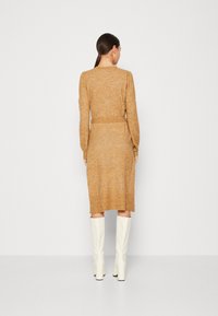 Rochie până la genunchi, cu mâneci lungi, din tricot muștar cu un finisaj texturat, având o talie evidențiată cu belt și o siluetă dreaptă, asortată cu cizme albe până la genunchi.