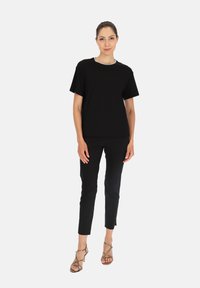 Czarny t-shirt z krótkim rękawem i okrągłym dekoltem, zestawiony z dopasowanymi czarnymi spodniami i sandałami na wysokim obcasie z wężowym wzorem.