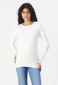 Maglietta bianca a maniche lunghe realizzata in tessuto morbido, con colletto rotondo e silhouette aderente, abbinata a jeans azzurri chiari.