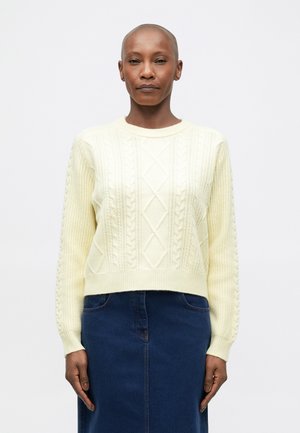 Pull en maille à chevrons jaune clair avec un col rond et un ourlet côtelé, présentant un motif en diamant et des manches texturées, assorti avec une jupe en denim.