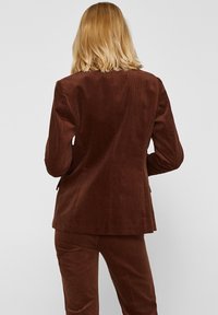 Blazer in velluto a coste marrone con una vestibilità su misura, caratterizzato da un design di lunghezza intermedia e una texture sottile, visto da dietro.