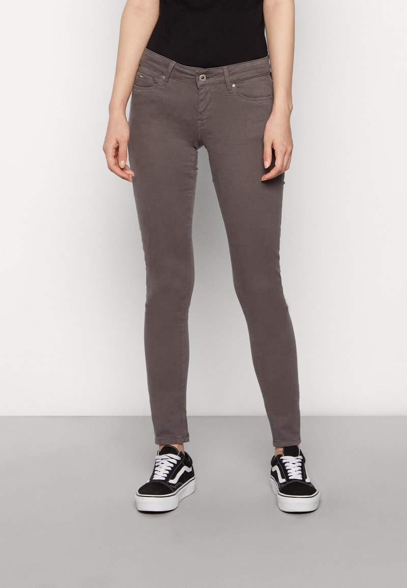 Jeans ajustados grises con una textura suave, que cuentan con cinco bolsillos y un cierre de cremallera. Combinados con zapatillas en blanco y negro.