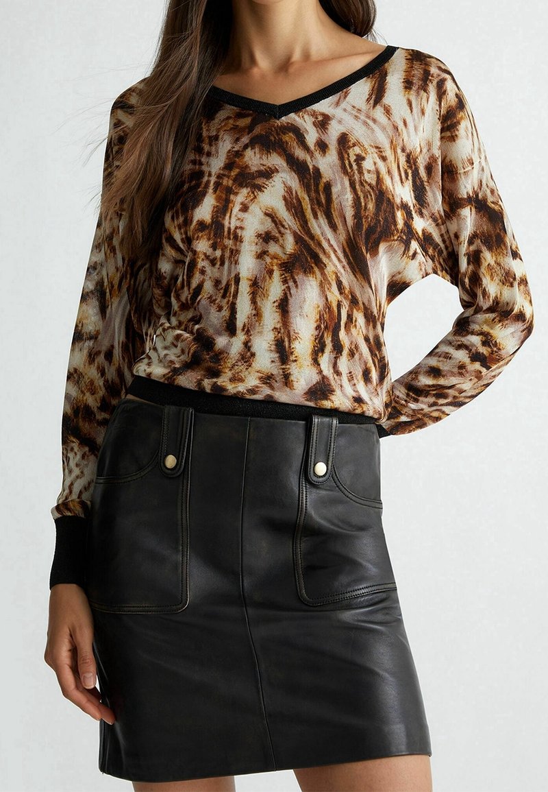 Langärmeliges V-Ausschnitt-Oberteil mit braun-cremigem abstraktem Muster, kombiniert mit einem schwarzen Leder-Minirock mit Fronttaschen und Druckknöpfen.