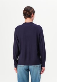 Tumesinine kudum sweater, millel on kerge lõike, soonikvarrukad ja ümaralune äär, kantud koos helesiniste sirgete pükstega.