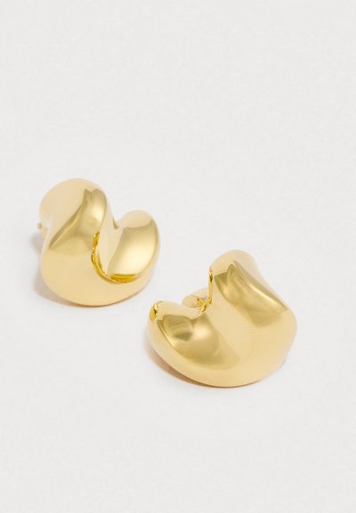 Zelta metāla auskari ar gludu, apaļu, abstraktu dizainu. Tie ir ar spīdīgu apdari un unikālu, asimetrisku formu.