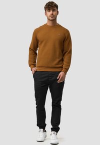 Brauner Sweatshirt mit Struktur und Rundhalsausschnitt, kombiniert mit schwarzen, taillierten Hosen und weißen Sneakern, mit elastischen Bündchen und Taschen.