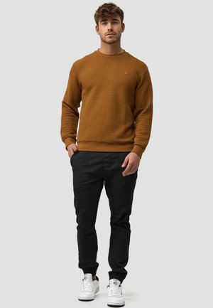Sweatshirt texturé marron avec un col rond, associé à un pantalon noir fuselé et des baskets blanches, avec des poignets élastiques et des poches.