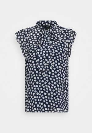 Marineblauwe mouwloze blouse met wit bloemmotief en een vastgeknoopt strikje aan de kraag.