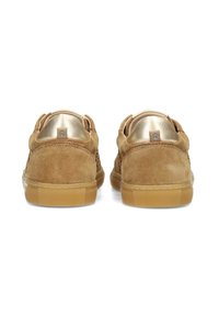 Zapatos de ante marrón con un perfil bajo, que presentan una suela texturizada en tono beige y acentos dorados en el tacón. Forro interior suave. Mínima visibilidad de la marca.