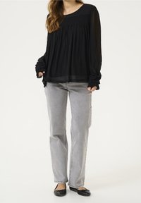 Blouse noire transparente à manches longues avec des détails froncés aux manches, associée à un jean gris clair droit et des ballerines noires.