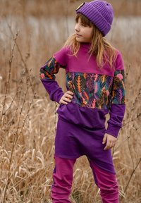 Fioletowa bluza z kolorowymi wzorami liści na piersi, w zestawie z fioletowymi spodnimi. Do tego fioletowa dzianinowa czapka.