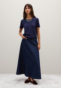 Maglietta a maniche corte blu navy abbinata a una lunga gonna in denim scuro. La gonna ha una linea dritta e una sottile cucitura sull'orlo. Scarpe marroni senza lacci.