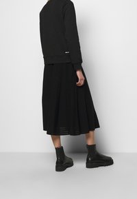 Svart sweatshirt med ribbade ärmar och nederkant, tillsammans med en svart plisserad midikjol. Skor: svarta ankelboots med tjock sula.