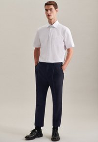 Witte korte mouwen overhemd met knopen en een borstzak, gecombineerd met marineblauwe broek en zwarte schoenen. Glad materiaal, getailleerde pasvorm, minimalistisch ontwerp.