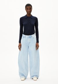 Donkerblauwe langemouwen polo met kraag en knoopsluiting, gecombineerd met lichtblauwe wijde jeans met gebogen naden en een relaxte fit.