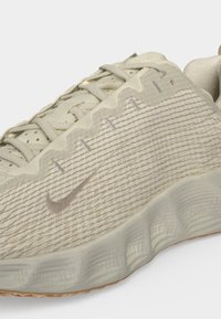 Μπεζ αθλητικό παπούτσι Nike με υφασμάτινο επάνω μέρος με υφή, κορδόνια, κυματιστή λεπτομέρεια στο πλάι και μαλακή σόλα.