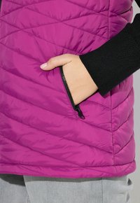 Rosa gestepptes Weste mit Reißverschlusstasche, ausgestattet mit einer strukturierten Oberfläche und schwarzen Strickärmel. Geometrisches Rautenmuster auf dem Stoff.