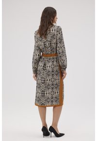 Czarna i kremowa sukienka w wzory z długimi rękawami, ściągnięta w talii, z brązowymi akcentami; do kolan, o gładkiej fakturze i dopasowanym kroju.