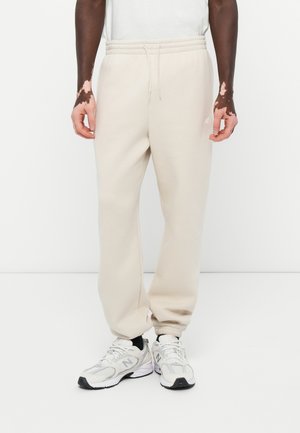 Beige Baumwoll-Sweatpants mit elastischem Bund und Seitentaschen. Kombiniert mit grauen New Balance Sneakern mit schwarzen Akzenten.