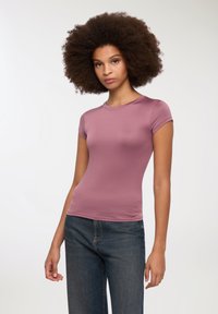 Top attillato a maniche corte in morbido tessuto malva, con scollatura rotonda e superficie liscia, abbinato a jeans blu scuro.