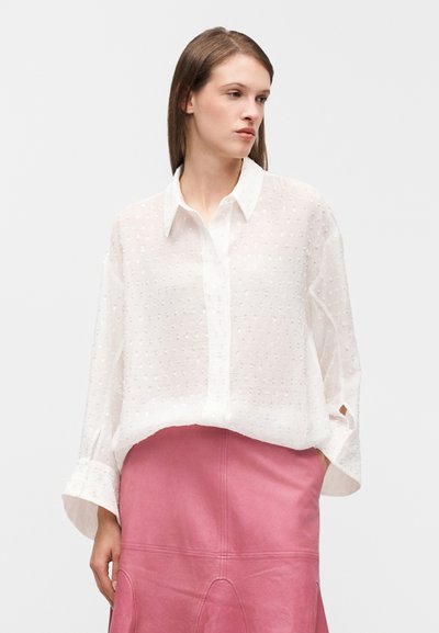 Λευκό, ημιδιάφανο πουκάμισο με μακριά μανίκια και κουμπιά, διακοσμημένο με μικρές κεντημένες τελείες, συνδυασμένο με ροζ δερμάτινη φούστα.