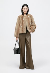 Krátká bunda z umělé kožešiny světle hnědé barvy se stříbrnými hvězdnými ozdobami, doplněná vysokým pasem hnědých kožených kalhot a černou kabelkou.