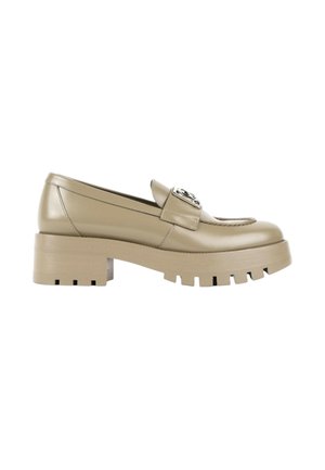Mocassin en cuir beige avec semelle crantée épaisse, talon bloc, détails cousus et emblème métallique décoratif sur la bride.