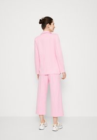 Un costume ajusté rose clair avec un col cranté et un pantalon à jambe large. Porté avec des baskets blanches à accents jaunes.