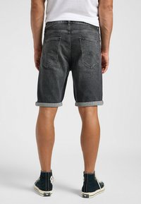 Pantalones cortos de mezclilla en gris oscuro con puños enrollados, cinco bolsillos y sutiles detalles de costura en la parte trasera. Llevados con zapatillas altas.