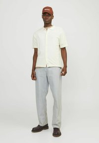 Heled kollane lühikeste varrukatega särk, nööbid ees. Heleda sinise laia säärega teksapüksid. Pruun müts valge tekstiga. Tumedad pruunid saapad.