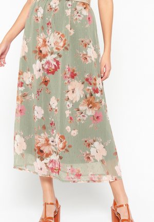 Grüner Midirock mit Blumenmuster in Pink, Weiß und Braun, kombiniert mit braunen Sandalen mit Blockabsatz und einem beigen Oberteil.