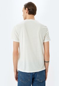 Helles beige T-Shirt mit kurzen Ärmeln, Rundhalsausschnitt, einer weichen Textur und einem lässigen Schnitt, kombiniert mit Jeans.