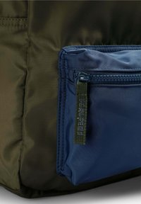 Bolsa de nailon en verde oscuro y azul marino con un acabado texturizado, que cuenta con un bolsillo con cremallera y un asa de bucle trenzado en el lateral.