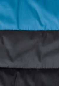 Tessuto testurizzato diviso in due sezioni orizzontali: la parte superiore è blu liscia, quella inferiore è nera opaca. Il materiale è leggero e resistente.