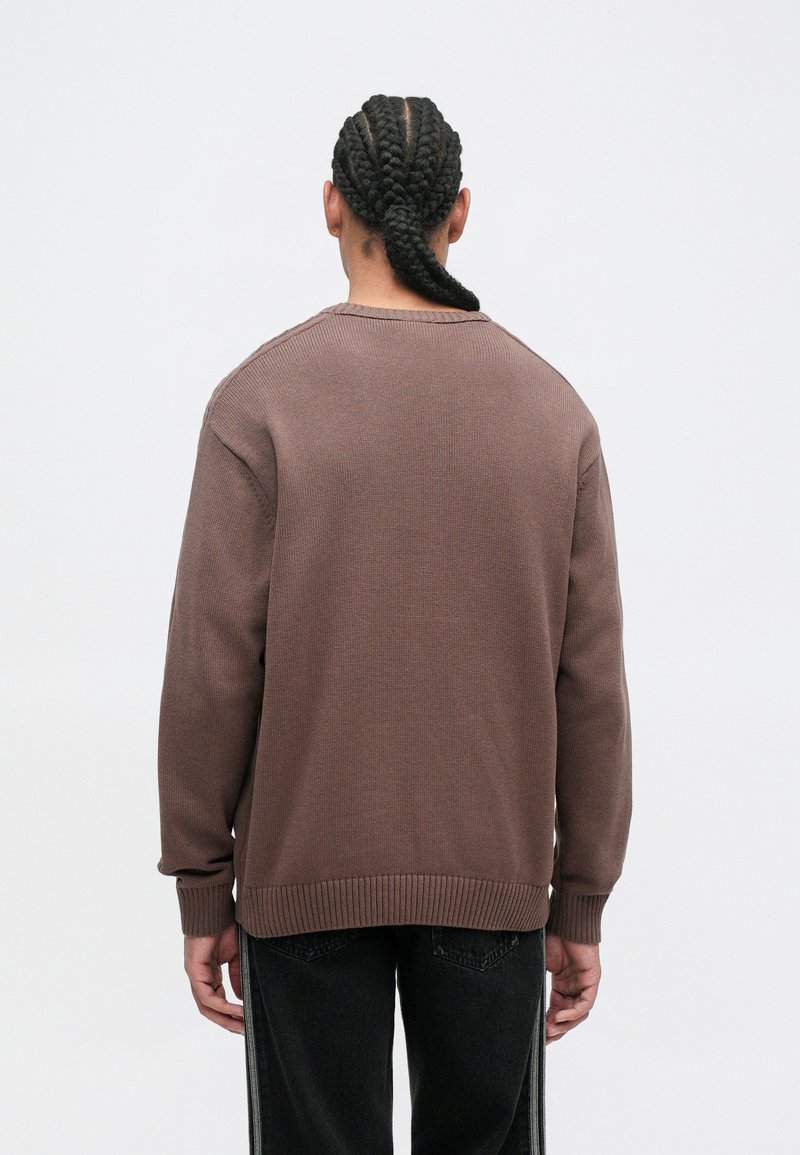Brown knit sweater with long sleeves, ribbed cuffs, and hem. The back features a rounded neckline and a textured pattern detail.