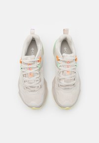 Ljusbeige sportskor med nät och texturerat material, med orangea och gröna accenter, en stabil sula och en dragband på hälen.