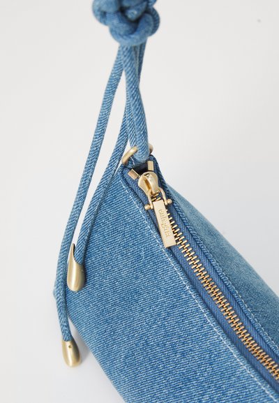 Denim pouch med guld lynlås, knyttet stofsnor og glat overflade. Har en trekantet form og metalliske accenter.