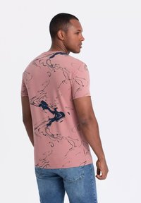 T-shirt rosa a maniche corte con un motivo blu navy ondulato. Realizzato in cotone, ha un design aderente e un collo tondo. Finitura texturizzata evidente.