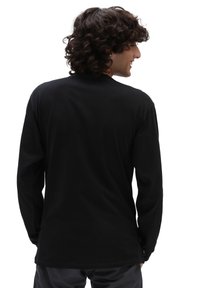 Tricou negru cu mânecă lungă, realizat dintr-un material moale și neted. Poate fi descris printr-un decolteu rotund și o croială lejeră, cu cusături laterale.