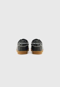 Black leather shoes with a gum sole, featuring white stitching and branding at the heel. Rounded design and smooth texture.