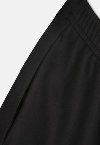 Schwarze Sportleggings mit einer glatten Textur, elastischem Bund und lässigem Design. Verfügt über eine Seitennaht für zusätzliche Details.