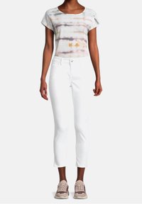 Pantalon capri blanc associé à un t-shirt tie-dye gris et multicolore. Les chaussures ont des accents roses et gris avec des lacets.